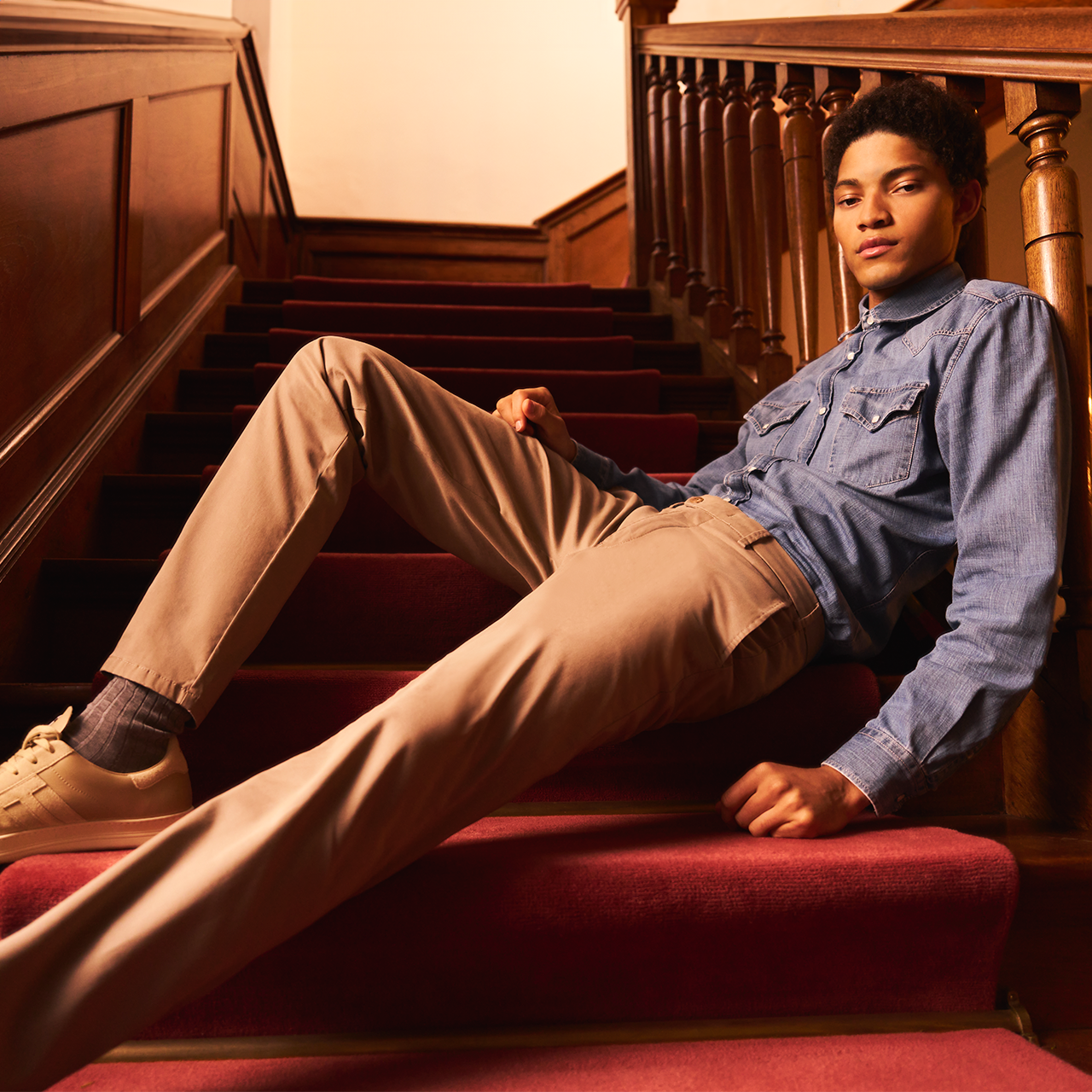 Man sitting on a staircase wearing a blue shirt and beige pants.